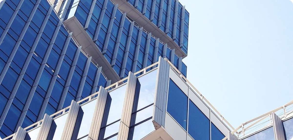 Modern building architecture with glass windows and angular design, reflecting a clear sky, emphasizing efficient HVAC and plumbing systems for comfort and maintenance.